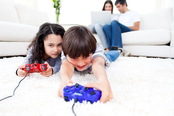 Glada barn som spelar TV-spel som ligger på golvet — Stockfoto