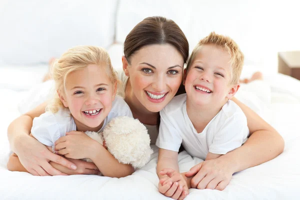 Happy mother and her children lying on a bed — Stock Photo, Image