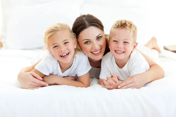 Laughing children playing with their mother lying on a bed — Stock Photo, Image