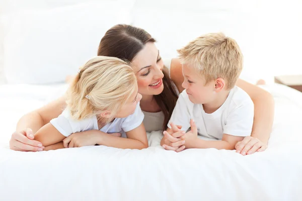 Joyeux enfants et leur mère discutant couché sur un lit — Photo