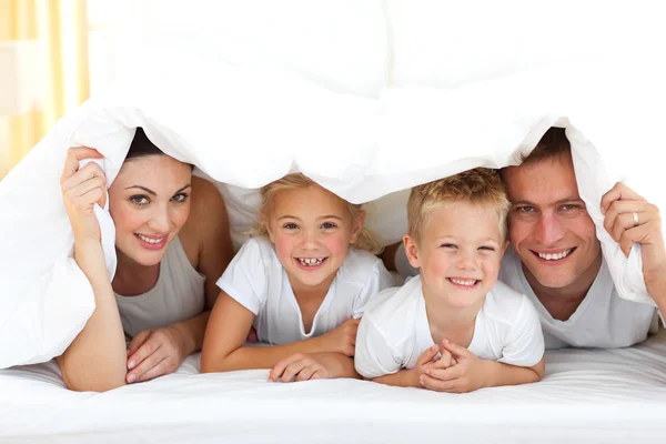 Ung familj spelar tillsammans på en säng — Stockfoto