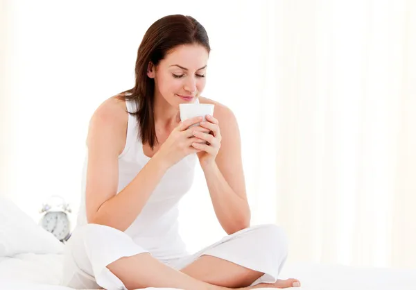 Entspannte Frau trinkt Kaffee sitzend auf ihrem Bett — Stockfoto