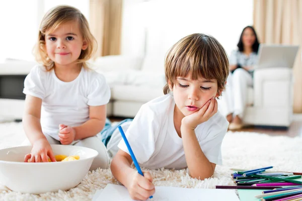 Серьезный маленький мальчик рисует и его сестра ест чипсы — стоковое фото