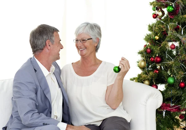 Mature couple sitting on sofa with a Christmas tree — Stock Photo, Image