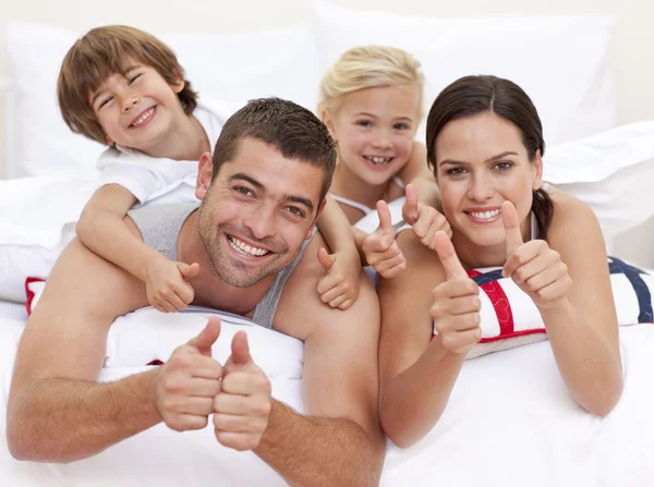 Família brincando na cama com os polegares para cima — Fotografia de Stock