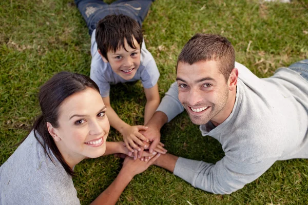 Rodiče a dítě ležící na zahradě s rukama dohromady — Stock fotografie