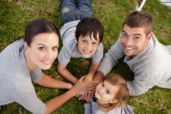 Молодые родители и дети, лежащие в саду с руками вместе — стоковое фото