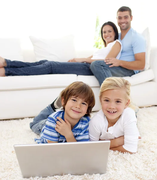 Дети играют с ноутбуком и родители лежат на диване — стоковое фото