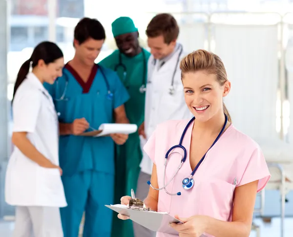 Blond sjuksköterska med sitt team i bakgrunden — Stockfoto