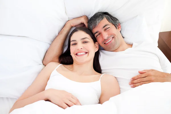 Sorridente coppia che abbraccia sdraiato nel loro letto — Foto Stock