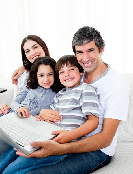 Jolly familia usando un ordenador portátil sentado en el sofá —  Fotos de Stock
