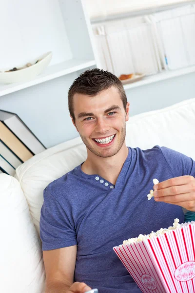 Красивый мужчина ест попкорн на диване — стоковое фото