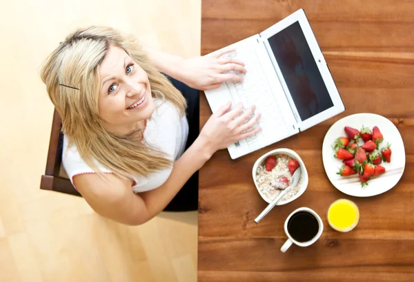 Mulher bonita usando um laptop enquanto toma café da manhã em casa — Fotografia de Stock