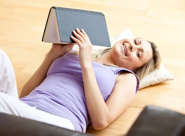 Wesoły kobieta czytająca książkę leżąc w salonie — Zdjęcie stockowe