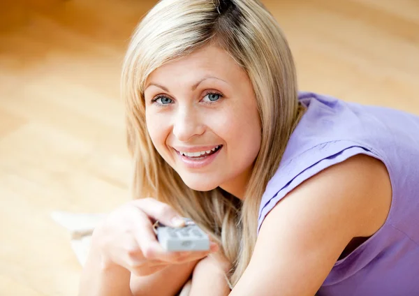 Mujer joven sonriente viendo la televisión tirada en el suelo en casa —  Fotos de Stock