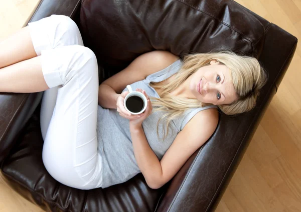 Affascinante donna che beve caffè seduta su un divano in soggiorno — Foto Stock