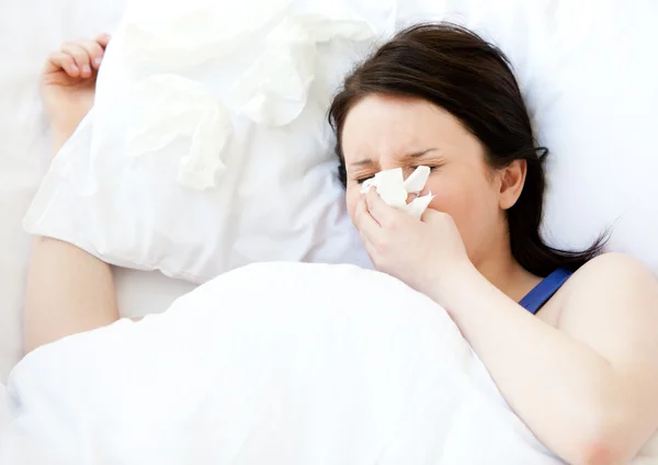 Άρρωστος νεαρή γυναίκα χρησιμοποιώντας έναν ιστό που βρίσκεται σε ένα κρεβάτι — Φωτογραφία Αρχείου