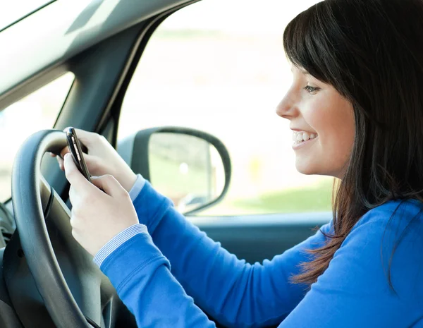 Morena jovem mulher escrevendo uma mensagem sentada em seu carro — Fotografia de Stock