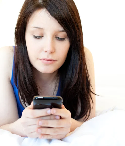 Concentrato giovane donna sms mentre sdraiato su un letto — Foto Stock