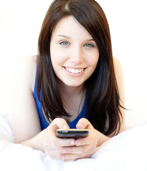 Happy young woman texting while lying on a bed — Stock Photo, Image