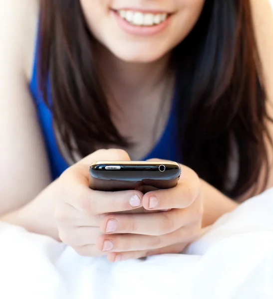 Close-up de uma adolescente morena mensagens de texto enquanto deitada em sua cama — Fotografia de Stock