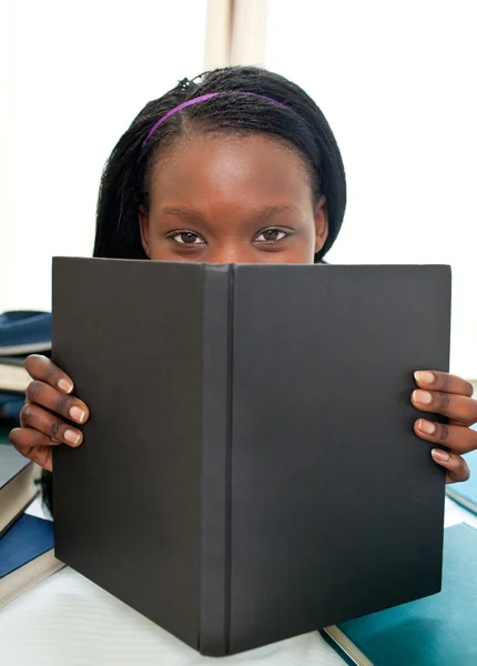 Χαριτωμένο αφρο-αμερικανικό έφηβος πίσω από ένα βιβλίο, κοιτάζοντας την κάμερα — Φωτογραφία Αρχείου