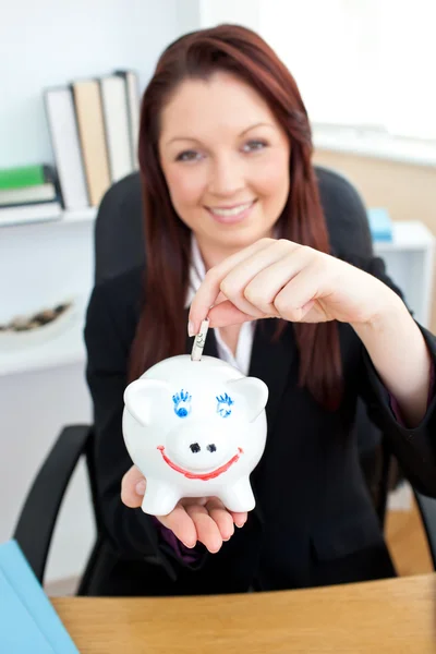 Self-assured young businesswoman putting money in a piggybank — Stock Photo, Image