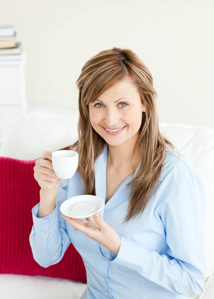 Glowing businesswoman holding a cup sitting on a sofa — Stock Photo, Image