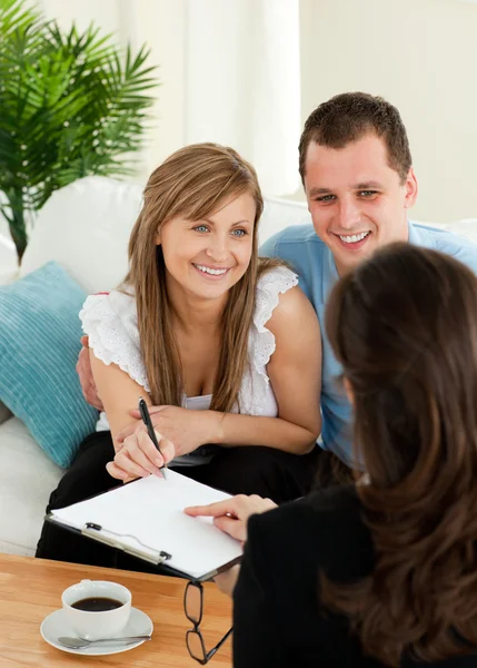 Happy young couple signing a contract sitting in the living room — Stock Photo, Image