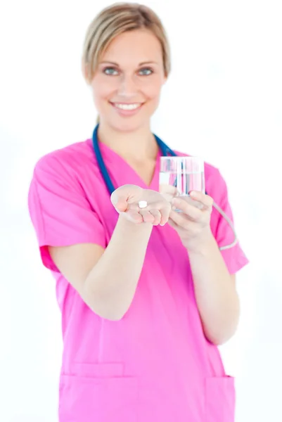 Brillante enfermera sosteniendo pastillas y un vaso de agua sonriendo en t —  Fotos de Stock