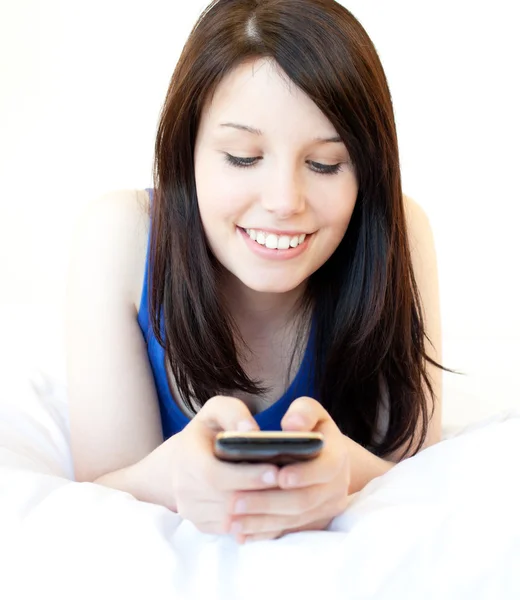 Happy female teenager using cellphone lying on the bed — Stock Photo, Image