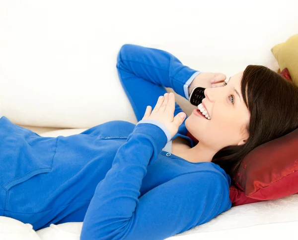 Surprised female teenager talking on phone lying on a sofa — Stock Photo, Image