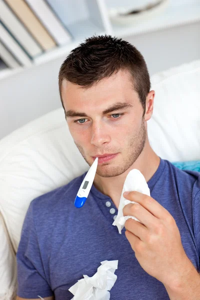 Morbid caucasian man sitting on the sofa with thermometer and ti — Stock Photo, Image