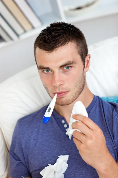 Sick caucasian man sitting on the sofa with thermometer and tiss — Stock Photo, Image