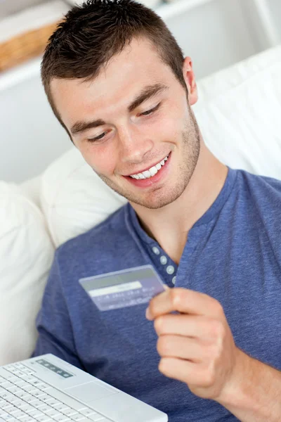 Çekici bir genç adam bir kart ve s üzerinde oturan bir latop holding — Stok fotoğraf