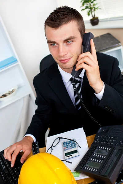 Caucasian young businessman talking on phone sitting at his desk — Stock Photo, Image