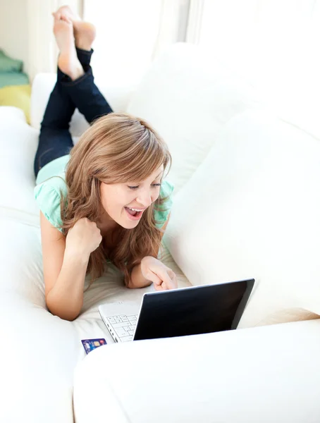 Весела біла жінка дивиться на свій ноутбук на дивані — стокове фото