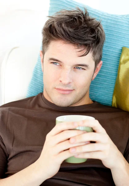 カリスマ的な若い男はソファに横になっているカップを保持しています。 — ストック写真