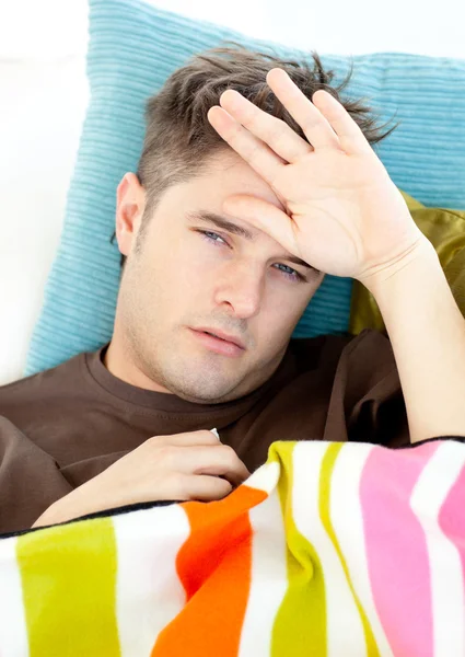 Jovem doente sentindo sua temperatura deitada no sofá — Fotografia de Stock