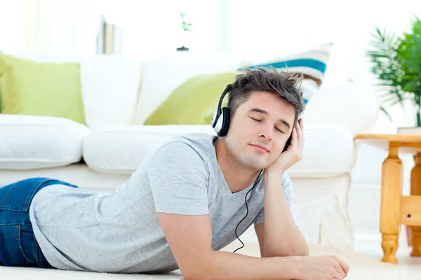 Charming young man listen to music lying on the floor — Stock Photo, Image