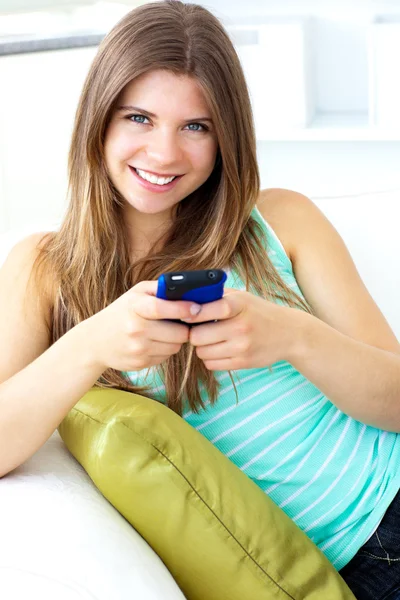 Sonriendo joven mujer mensajes de texto sentado en el sofá —  Fotos de Stock