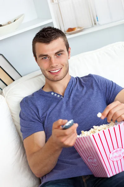 Очаровательный молодой человек ест попкорн перед телевизором — стоковое фото
