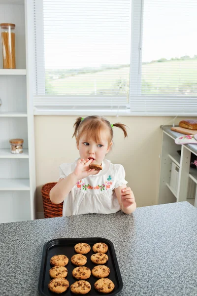 Menina bonito sentado na frente de biscoitos — Fotografia de Stock