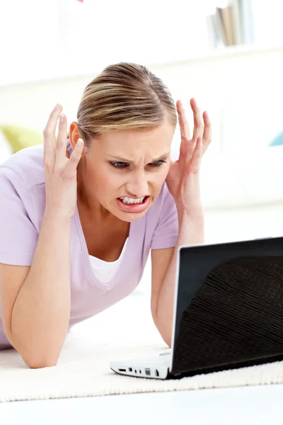 Mujer joven enojada tirada en el suelo usando su computadora portátil — Foto de Stock