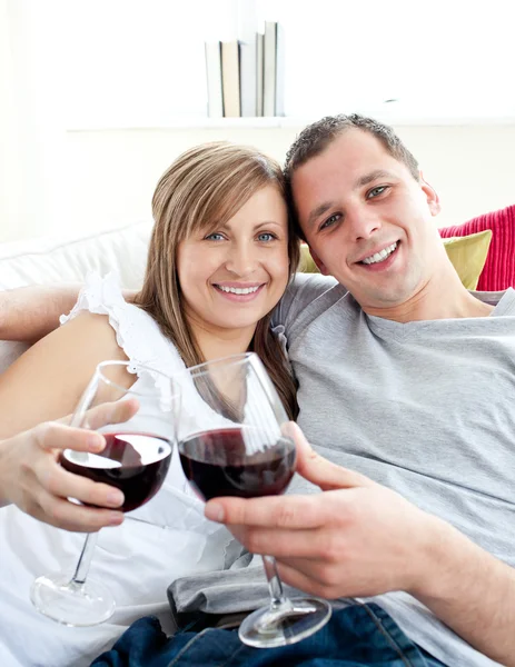Любящие молодые пары пьют вино сидя на диване — стоковое фото