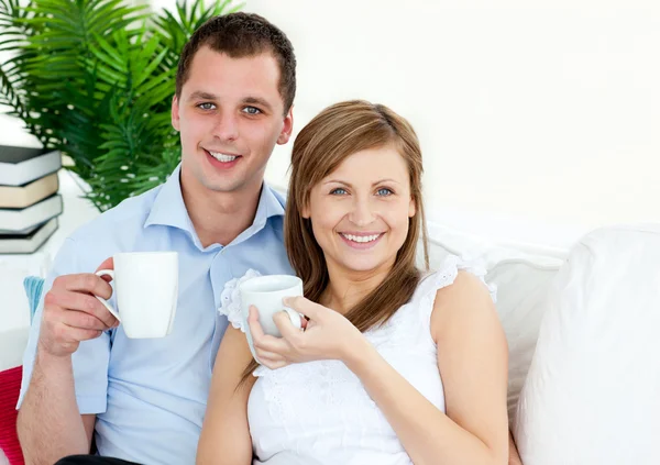Wesoła, młoda para, picie kawy siedząc na kanapie — Zdjęcie stockowe