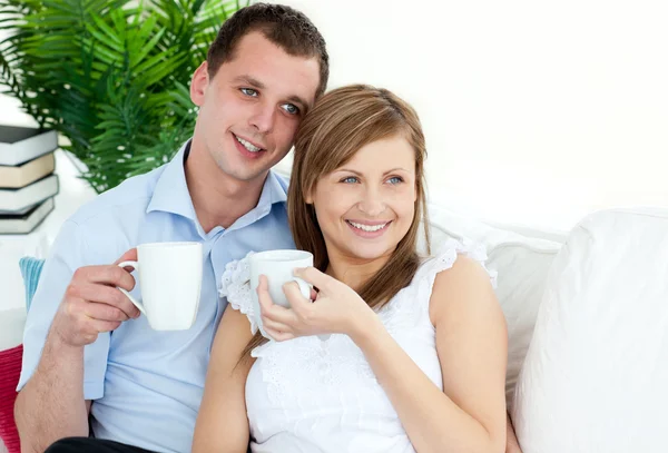 Jovem casal atento bebendo café sentado em um sofá — Fotografia de Stock