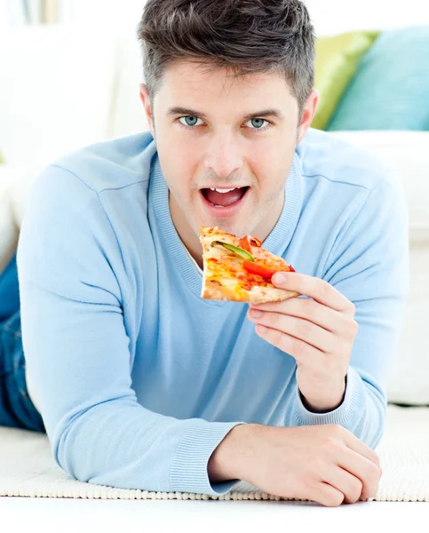 Молодий чоловік лежить на землі і їсть піцу — стокове фото
