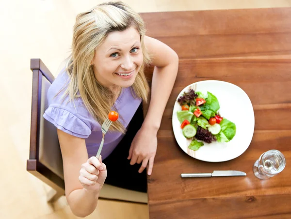 Portret van een mooie vrouw die het eten van een salade in de woonkamer Stockafbeelding