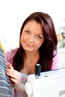 Attractive young caucasian woman sewing in the kitchen clipart